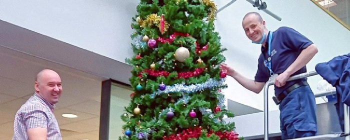 school staff standing on ladders decorating a large Christmas tree and smiling